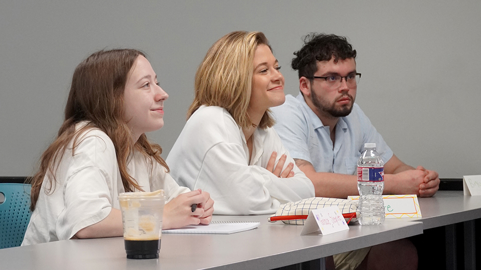 Students at a classroom table listening to a lecture