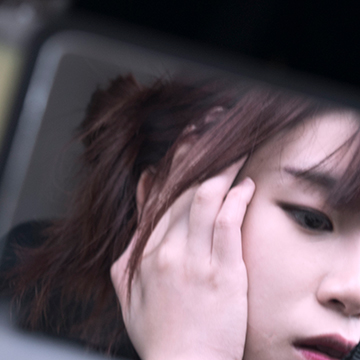 Image of a girl's face with her hand on the side of her face as seen through a car's side mirror