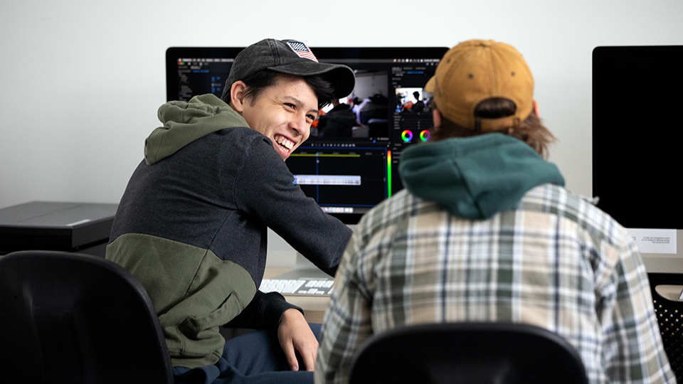 Two students laughing while working with film editing software on a computer