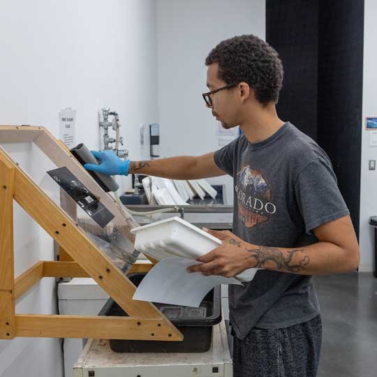 Student using a squeegee on a contact sheet in the analog photography studio