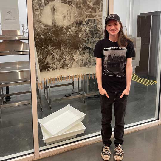 Proud student standing by their silver gelatin mural of a self-portrait