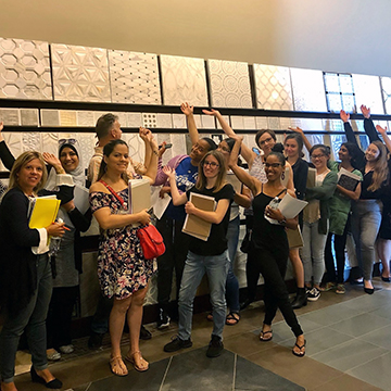 Happy ITMD students standing in front of a sample wall, waving their hands