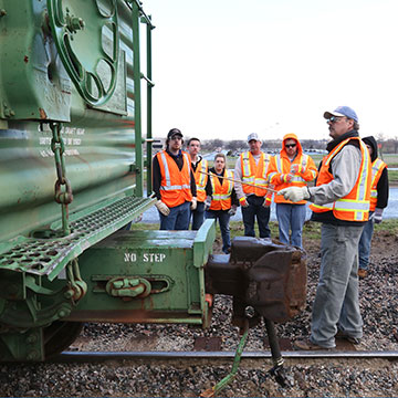 An instructor points out items on a rail car to a group of students.
