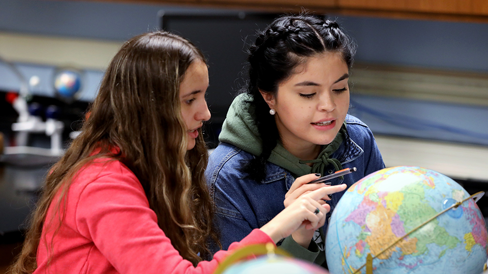 Two students studying a globe in a geosciences class