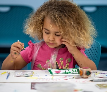 A young girl concentrates on a crayon drawing.