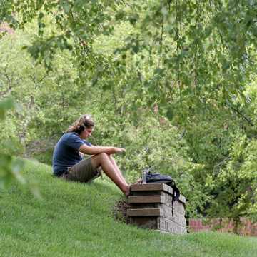 A student sits on the hill on campus and listens to music through headphones.