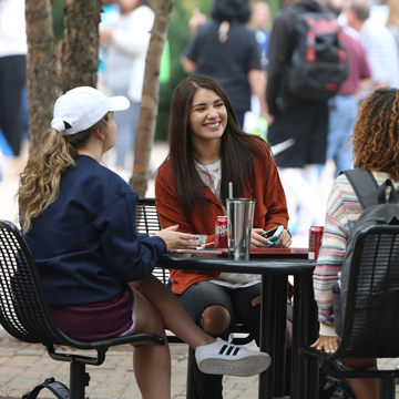 Three women sit at a picnic table to visit.