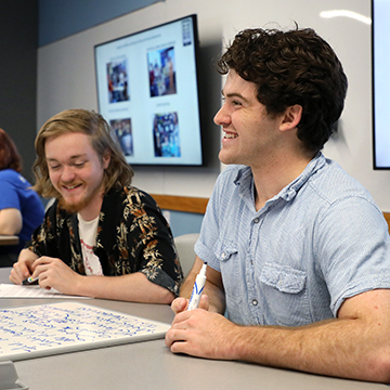 Two male students smile while in class. 