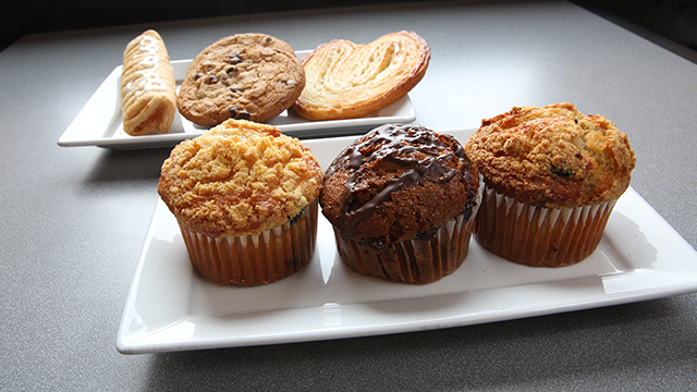 A plate of cookies in the background; a plate of 3 muffins in the foreground