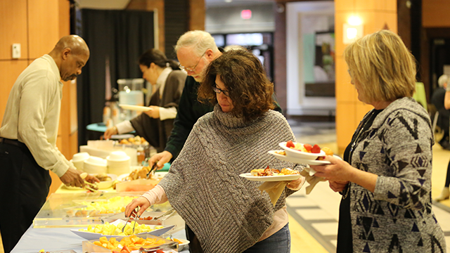 Buffet table with a variety of breakfast dishes. People are in line and serving themselves.