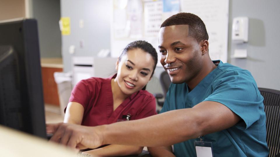 A male healthcare worker pointing out something on a monitor to a female healthcare worker