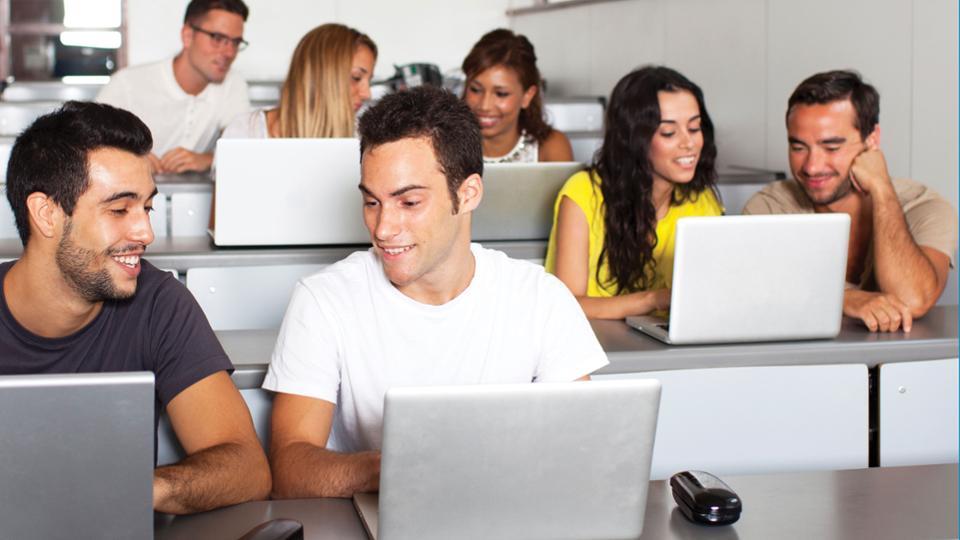 A classroom full of students working together at laptops