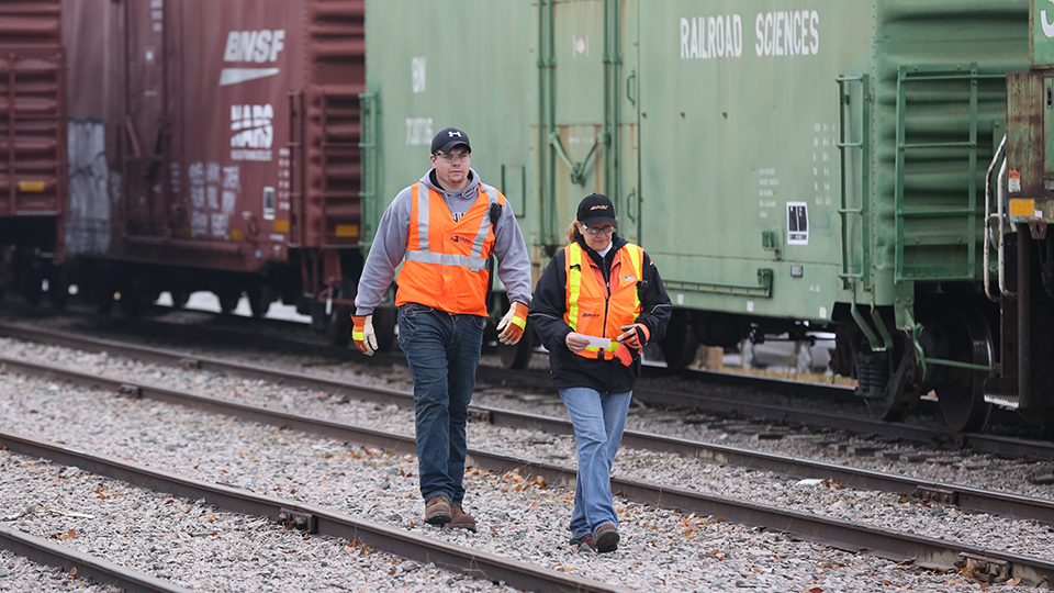 Two National Academy of Railroad Science students walking between the rails of a track in the simulated rail yard on the JCCC campus.