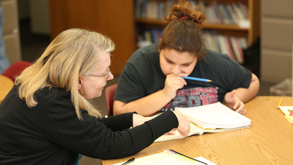 A female JCAE volunteer reviews material in a textbook with a female student