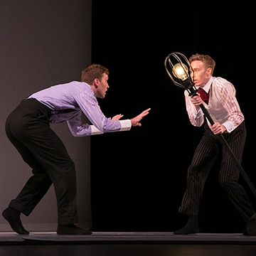 One man crouches down while a second man gestures at him with a lamp post.