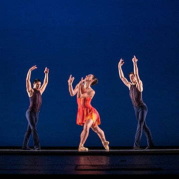Three modern dancers pose with their arms stretched upward.