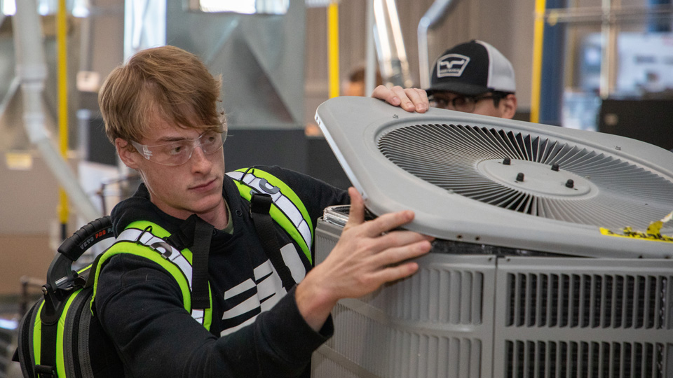 An HVAC student looks into an air conditioner.