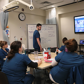 a group of nursing students meet around a table in the simulation center