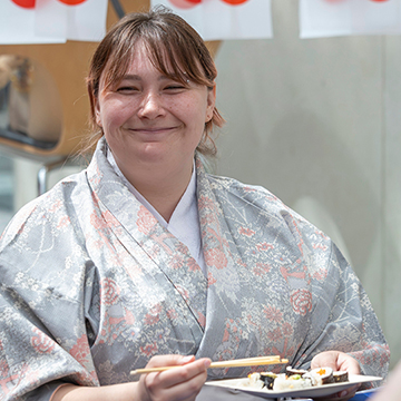 a smiling student wearing Japanese clothing eats with chop sticks