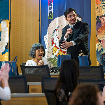 A presenter standing in front of Japanese artwork banners talks to participants at the Shorts Festival at JCCC