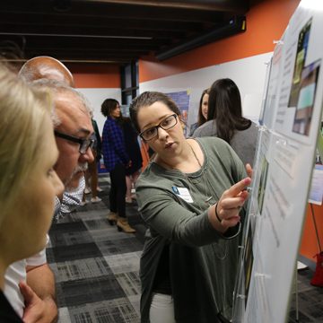 A student shares research from a poster presentationto two attendees at the Science and Math Poster Symposium.