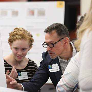 Two attendees look close at a poster at the Science and Math Poster Symposium.