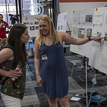Student in blue dress defends their work presented during the symposium.
