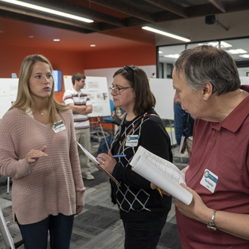 Two attendees listen as a student discusses their work at the symposium.