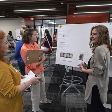 Student in gray sweater presents their work at the symposium.