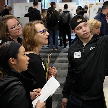 Three faculty members look on at work presented during the symposium.