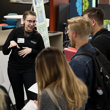 Student explains their work to three attendees at the symposium.