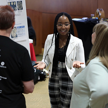 A student explains her research to two STEM Poster symposium attendees