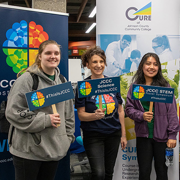 3 students and a professor hold up signs that say STEM Poster Symposium