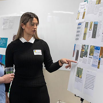 a female student points at her poster while explaining a concept to a symposium attendee