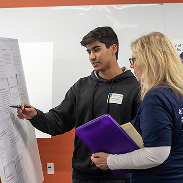 a male jccc student explains his poster to one of the judges who is listening intently