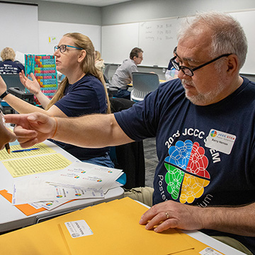 two event organizers wearing STEM poster symposium t-shirts sit at a desk and help check participants in