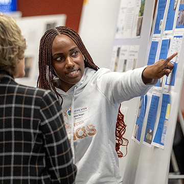 A JCCC student looks intently and points to her research displayed on a poster