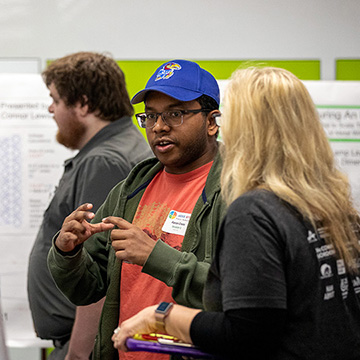 A young man explains his poster to a judge at the STEM Poster Symposium at JCCC