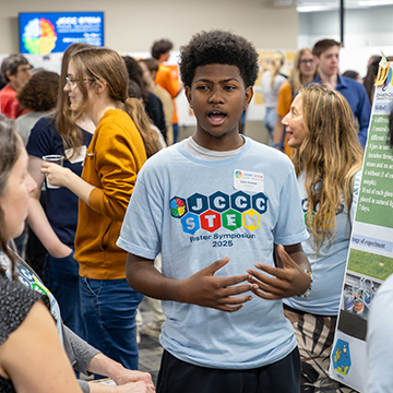 a young man explains his research findings at the 2025 JCCC STEM Poster Symposium