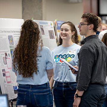 participants listen intently to a student presenting her research at the STEM Poster Symposium