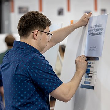 a student putting a printout on his poster display at the symposium