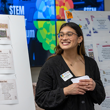 a smiling jccc student stands next to her poster at the STEM Poster Symposium