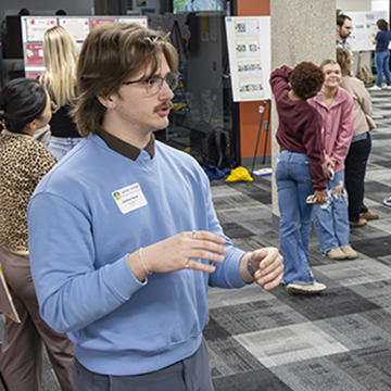 a student presents his poster to symposium attendees
