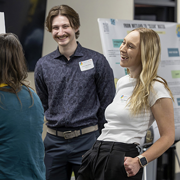 two smiling students talk to stem poster symposium presenter about her work