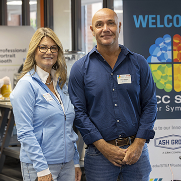 two representatives from symposium sponsor Ash Grove pose for a picture in front of a colorful STEM poster symposium banner