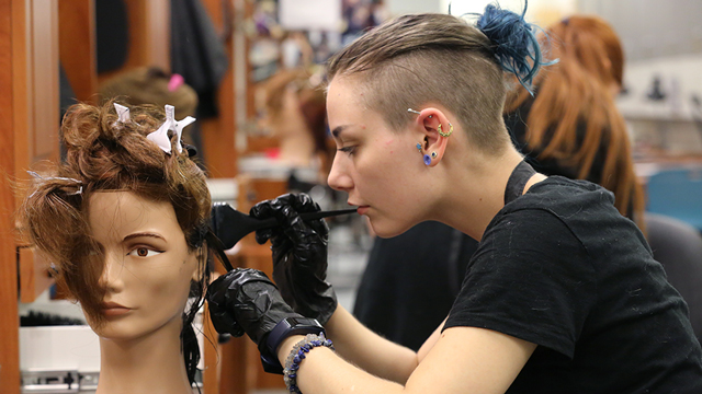 A cosemtology student applies hair color to a mannequin.