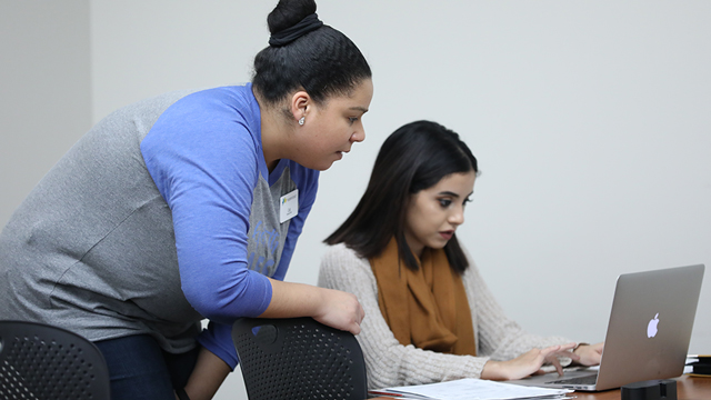 A JCCC employee helps a student with a MacBook.