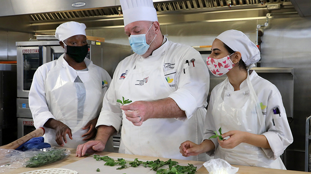 Two students and a chef/instructor examine some herbs.