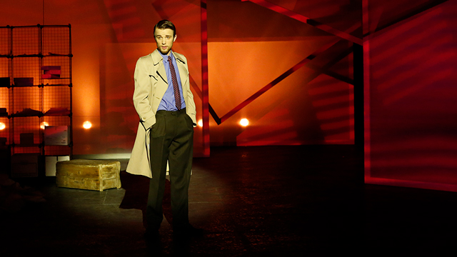 An actor wearing a trenchcoat on a stage.