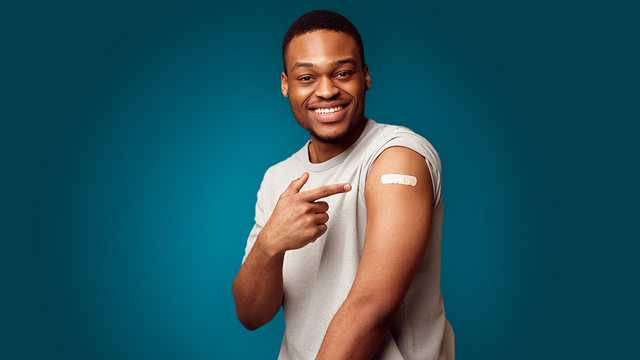 A smiling man rolls up his sleeve to show he got vaccinated.